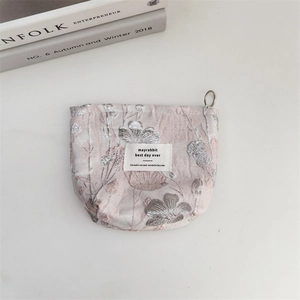 Flat lay of pale pink makeup bag with silver floral embroidery on white tabletop
