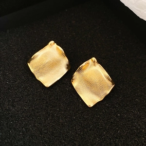 Gros plan de boucles d'oreilles dorées plissées irrégulières avec texture métal