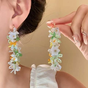 Detail of beaded floral tassel earrings with white flowers and green beads on model