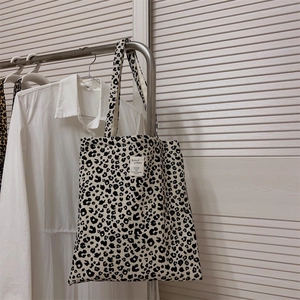Close-up of leopard print canvas tote bag with woven label hanging on a metal rack