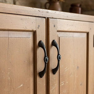Retro cast iron door handle with floral relief on vintage wooden cabinet door surface