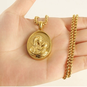 Gros plan du pendentif Vierge Marie doré sur chaîne à billes tenu à la main
