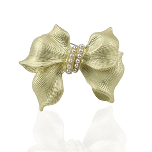 Elegant gold bow brooch with white pearls featuring a brushed metal texture and mirror reflection