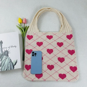 Detailed close-up of beige knitted tote bag with pink heart and diamond patterns on white fabric