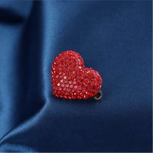 Macro shot of red heart rhinestone brooch pinned on elegant dark blue satin fabric