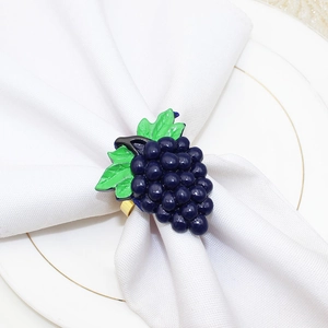 Detailed view of a purple grape napkin ring with gold finish on a white fabric