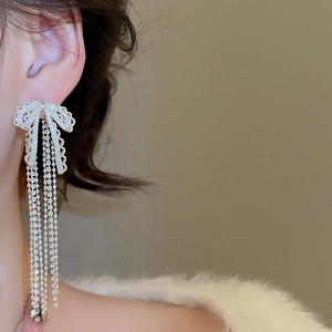 Close-up of a silver bow earring with long tassels and zircons on a model's ear