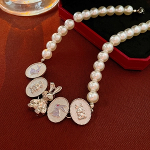 Dettaglio di collana di perle con ciondoli a coniglio su tessuto rosso vintage