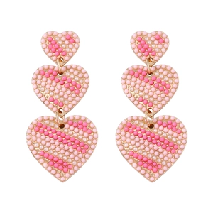 Close-up of dangling heart earrings with pink striped beads and gold-tone finish