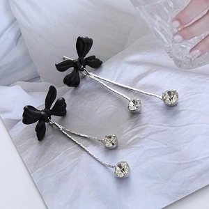 Détail de boucles d'oreilles papillon à pompons avec nœuds noirs sur tissu blanc texturé