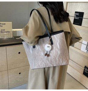Dettaglio di una borsa tote beige grande con texture a pieghe e ciondolo a pompon nero