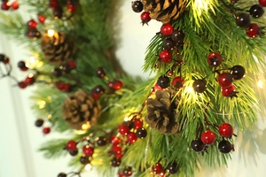 Close-up of Christmas wreath with red berries, pine cones and warm LED string lights