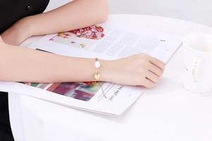 Détail d'un bracelet en chaîne dorée avec perle blanche et cœur poli sur le poignet d'un mannequin