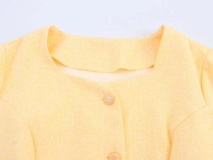 Dettaglio ravvicinato del tessuto tweed giallo con bottoni tondi e scollo quadrato