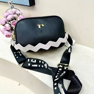 Detail of black pebbled leather crossbody bag with white wavy trim and gold T-logo
