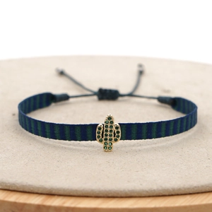 Bohemian woven strap bracelet with gold cactus charm and green crystals on wooden stand