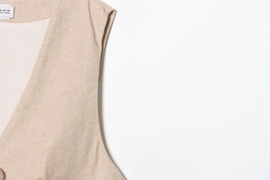Detail of beige linen sleeveless vest showing fabric texture and neck label with size S