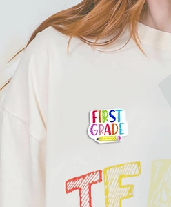 Detail of colorful First Grade teacher brooch with pencil design on white sweatshirt