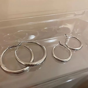 Detailed comparison of large and small round silver hoop earrings on a transparent surface