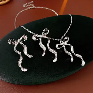Silver bowknot jewelry set featuring a polished necklace and earrings on green velvet