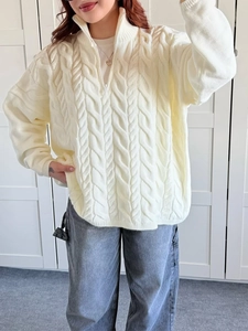 Detail of white cable knit sweater with half-zip collar worn by a model in soft light