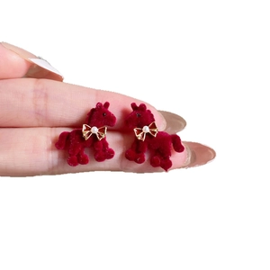 Red flocked pony earrings with golden bow and pearl detail on a white background