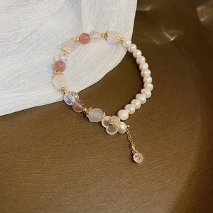 Detailansicht eines Perlenarmbands mit weißen Perlen, rosa Kristallen und Blumenanhänger