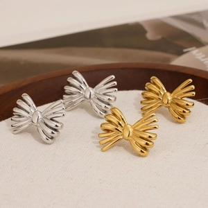Golden and silver stainless steel bow knot stud earrings on a rustic wooden tray