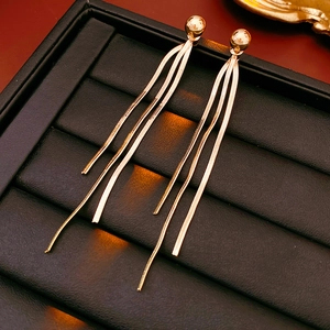 Makro-Detail von goldenen Schlangenkette-Quastenohrringen auf schwarzer Lederstruktur