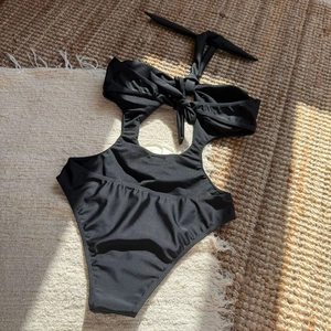 Detail of black cut-out one-piece swimsuit with halter neck and bow on textured rug