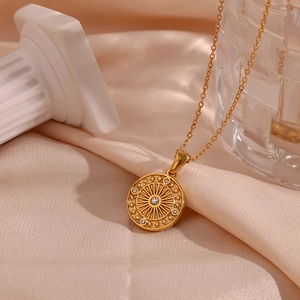 Detail of gold compass pendant with sparkling zircons on elegant champagne silk fabric
