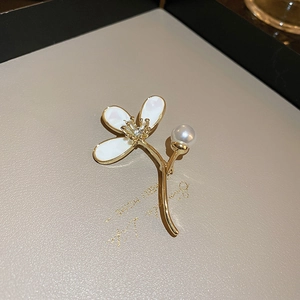 Vue détaillée d'une broche fleur dorée avec perles, zircons et pétales en émail blanc
