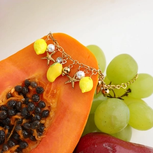 Macro shot of 18K gold plated bracelet with lemon and pearl charms on fresh fruit