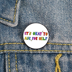 Macro shot of 'IT'S OKAY TO ASK FOR HELP' enamel pin on blue denim fabric background