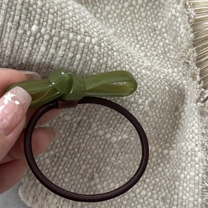 Detailed shot of a green acetate bow hair tie with a brown elastic band held in hand