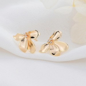Elegant gold flower stud earrings with zircon center on a soft white fabric background