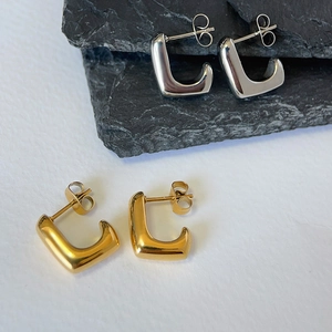Detailed view of minimalist gold and silver C-shaped hoop earrings on textured stone