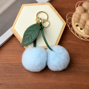 Detail of light blue faux rabbit fur cherry keychain with green leaf and golden metal hardware