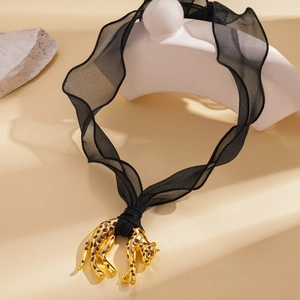 Detail of a black wavy mesh choker with a 3D gold leopard pendant on a textured stone