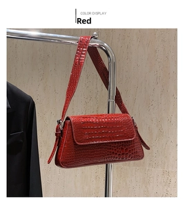 Detail of red crocodile pattern shoulder bag hanging against a textured wall