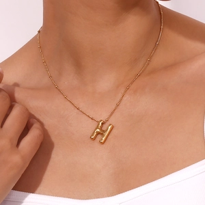 Minimalist gold necklace with 3D H-letter pendant worn by model on white background