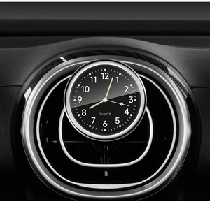 Luminous quartz car clock mounted on dashboard vent with black dial and white numbers