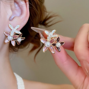 Detailed shot of floral stud earrings featuring 18K gold plating and pearl accents