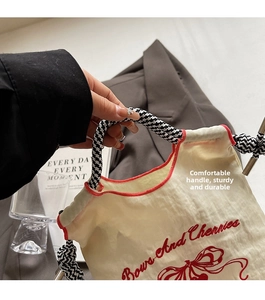 Close-up of cream nylon bag with red bow embroidery and checkered woven handle
