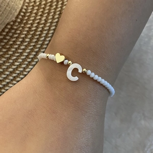 Detail of beaded bracelet with gold heart and C initial charm on a person's wrist