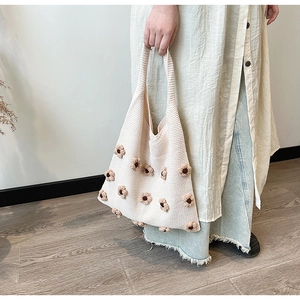 Detail view of cream knitted tote bag featuring three-dimensional brown floral crochet accents
