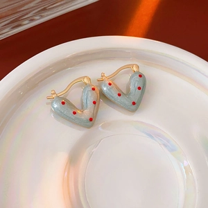 Macro detail of heart-shaped earrings with grey enamel and red polka dots on ceramic tray