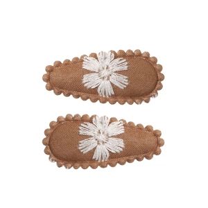 Detail of two handmade brown fabric hair clips with white floral embroidery and scalloped edges