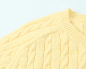 Detail of light yellow knit sweater showing round neck and cable knit texture pattern