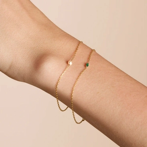 Detailed shot of a delicate gold chain bracelet featuring an oval green zircon stone